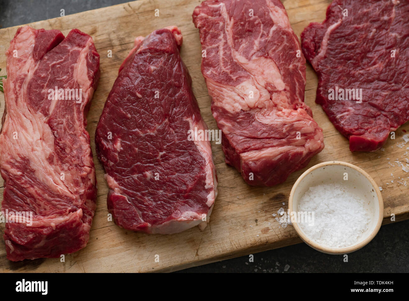 Raw black angus prime beef steak variety on vintage cutting board with rosemary, sea salt and spices Stock Photo