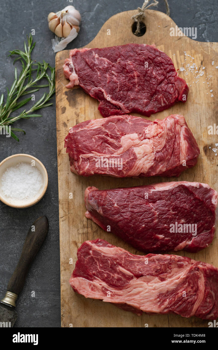 Raw black angus prime beef steak variety on vintage cutting board with rosemary, sea salt and spices Stock Photo