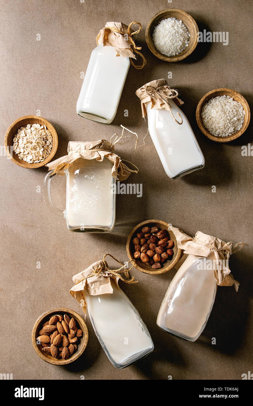 Variety of non-dairy vegan lactose free nuts and grain milk almond, hazelnut, coconut, rice, oat in glass bottles with ingredients above over brown te Stock Photo