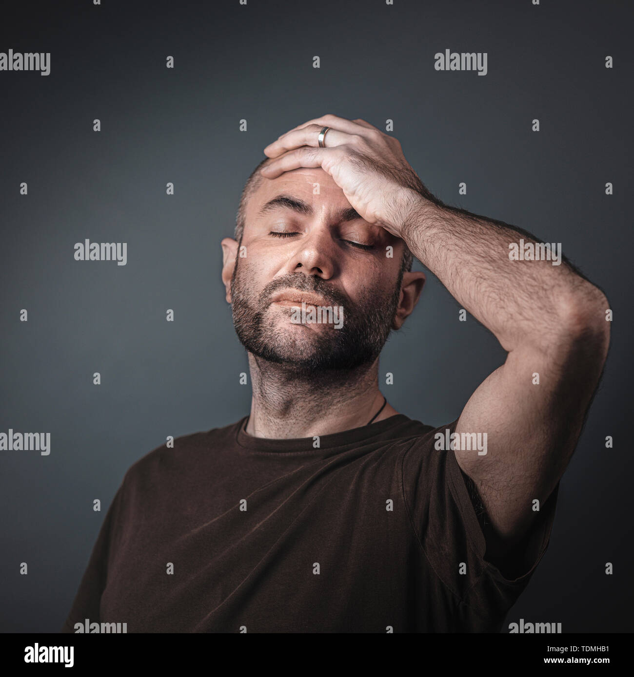 portrait of caucasian man with beard and short shackles, hand on forehead and eyes closed. Studio shot. Stock Photo