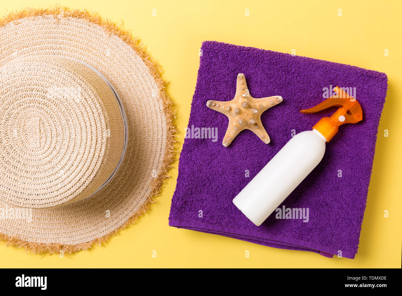 Beach flat lay accessories with copy space. Violet towel, seashells, staw sunhat and a bottle of sunblock on yellow background. Summer holiday concept Stock Photo