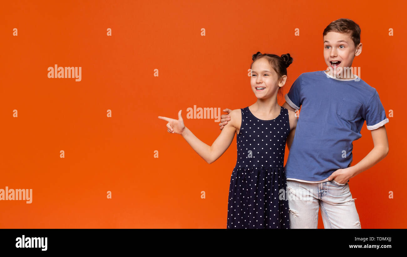 Amazed kids pointing aside at empty space, orange background Stock Photo