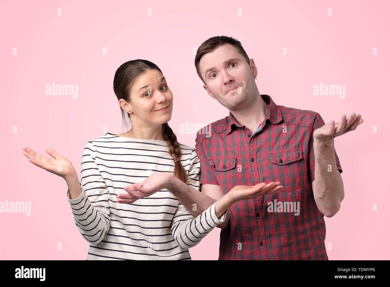 Uncertain couple shrugging shoulders isolated over pink background Stock Photo