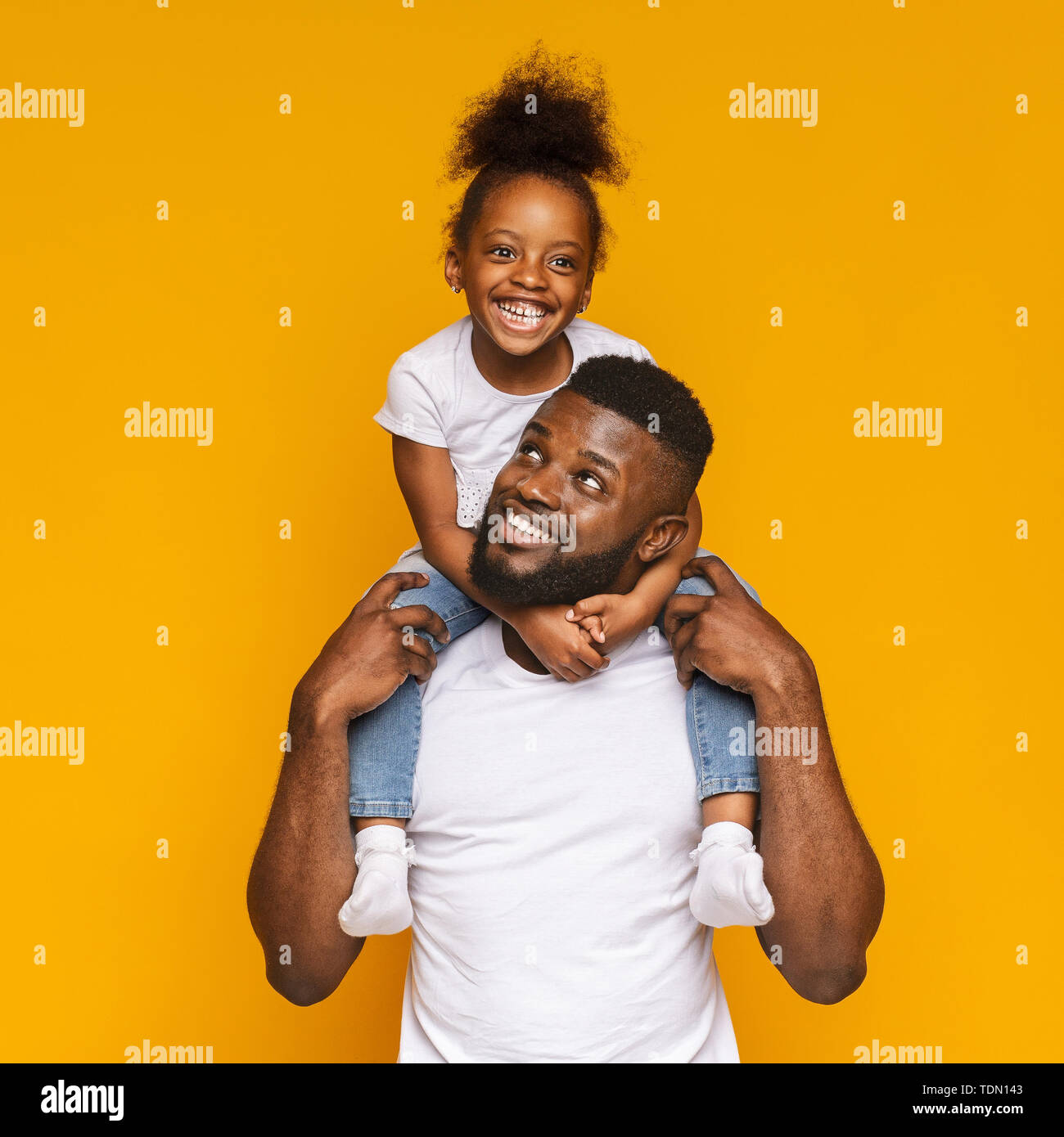 Cheerful black man riding his cute little daughter on shoulders Stock Photo