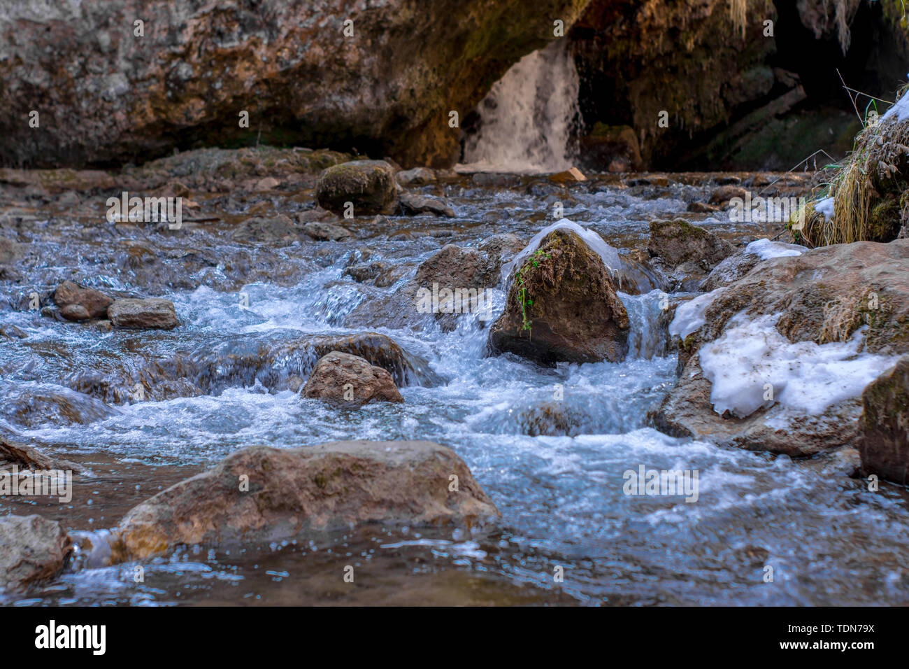 Cold mountain river flows between stones with snow and ice, selective focus, waterfall in the background, Karachay-Cherkess Republic. Stock Photo