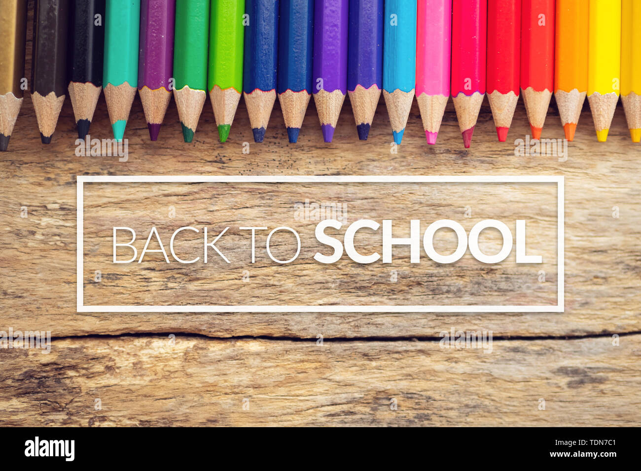 colorful color pencils on old wooden background table with text back to school in white border frame Stock Photo