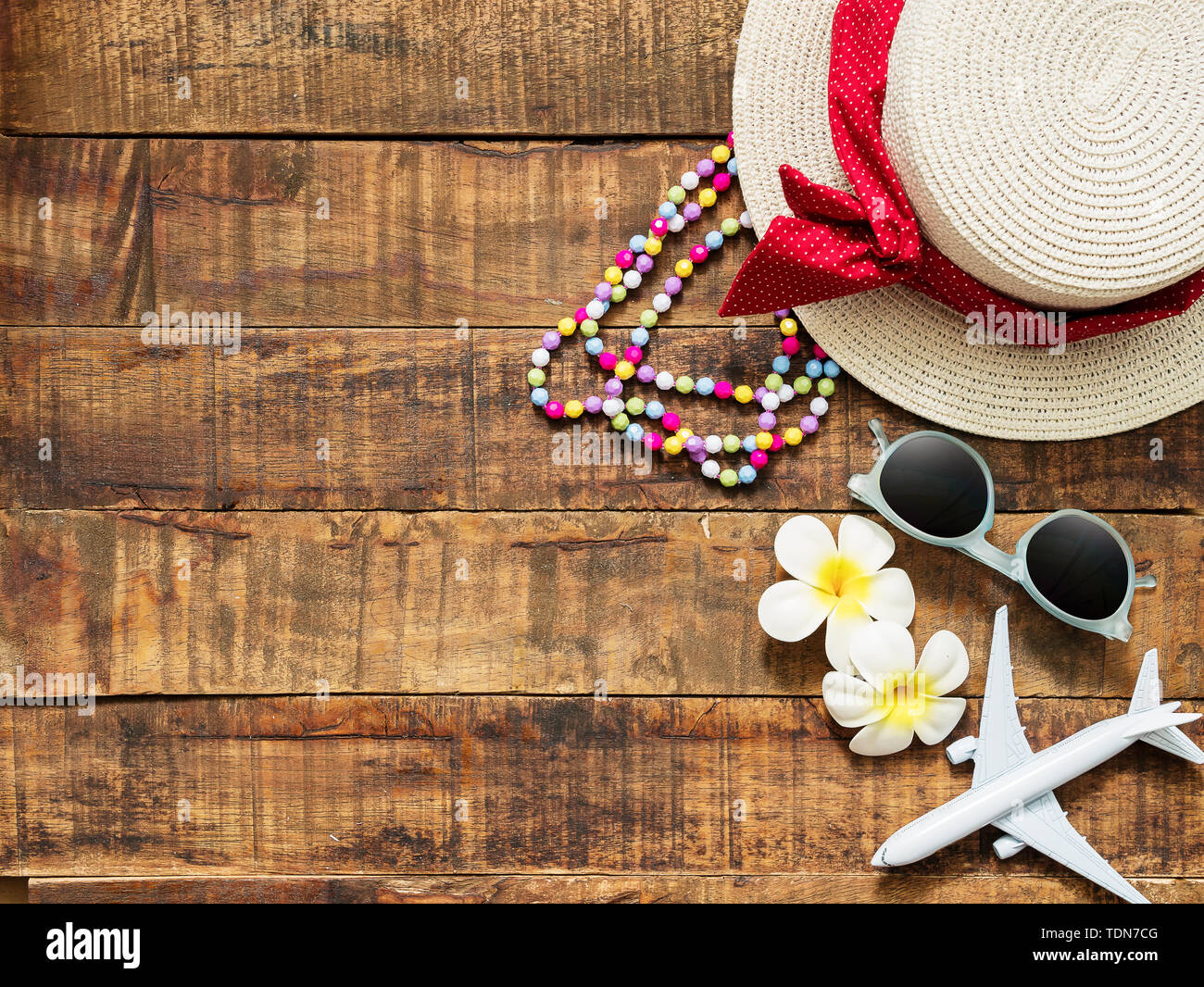flat lay of hat , necklace , sun glass , flower and red heart shape as traveler's accessories items for summer vacation and plane model on wooden back Stock Photo