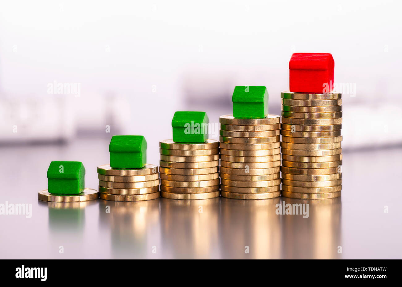 Rising stacks of coins, four green cottages and a red house Stock Photo