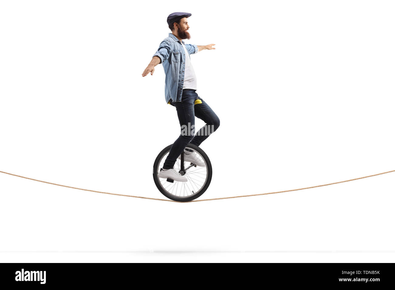 Full length shot of a young man riding a unicycle on a rope and balancing with hands isolated on white background Stock Photo