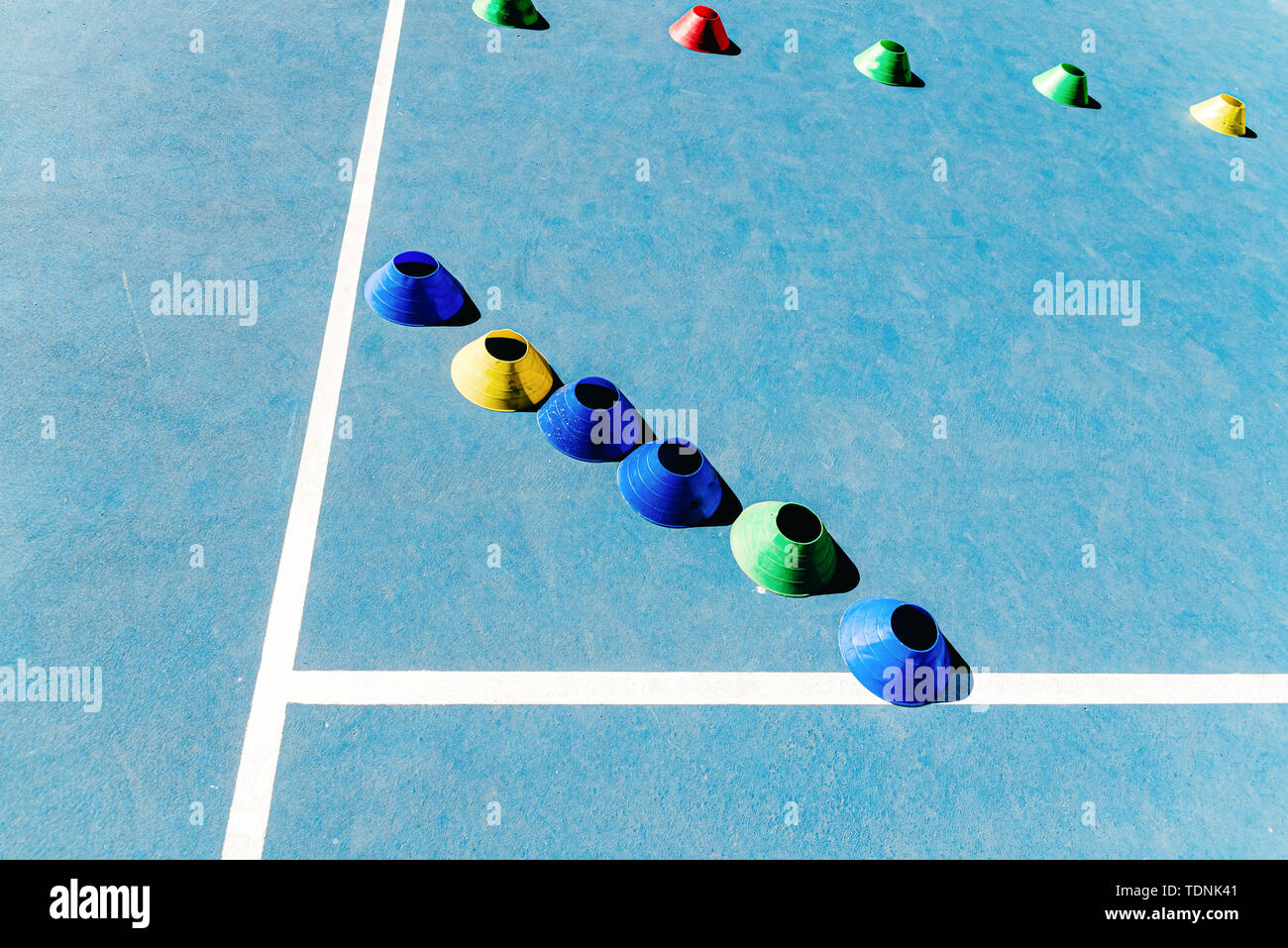 Colorful plastic cones on a blue cement tennis court with white lines