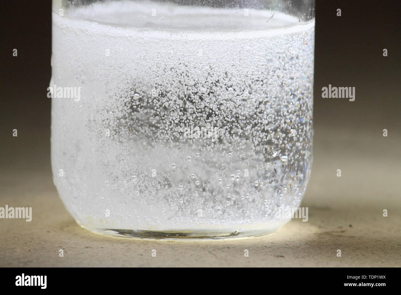 Closeup of a vinegar and baking soda reaction happening in the bottom of a glass jar; violent reaction with many bubbles Stock Photo