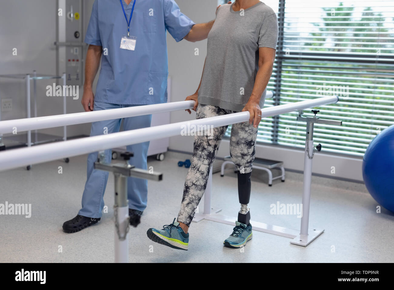 Male physiotherapist helping patient walking with parallel bars in the hospital Stock Photo