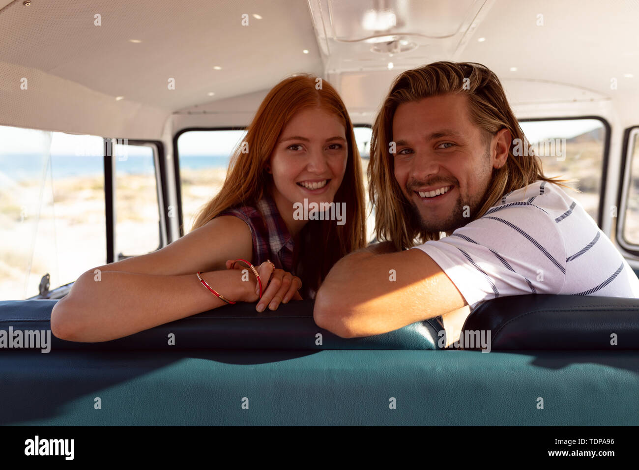 Happy young couple looking at camera in front seat of camper van at beach Stock Photo