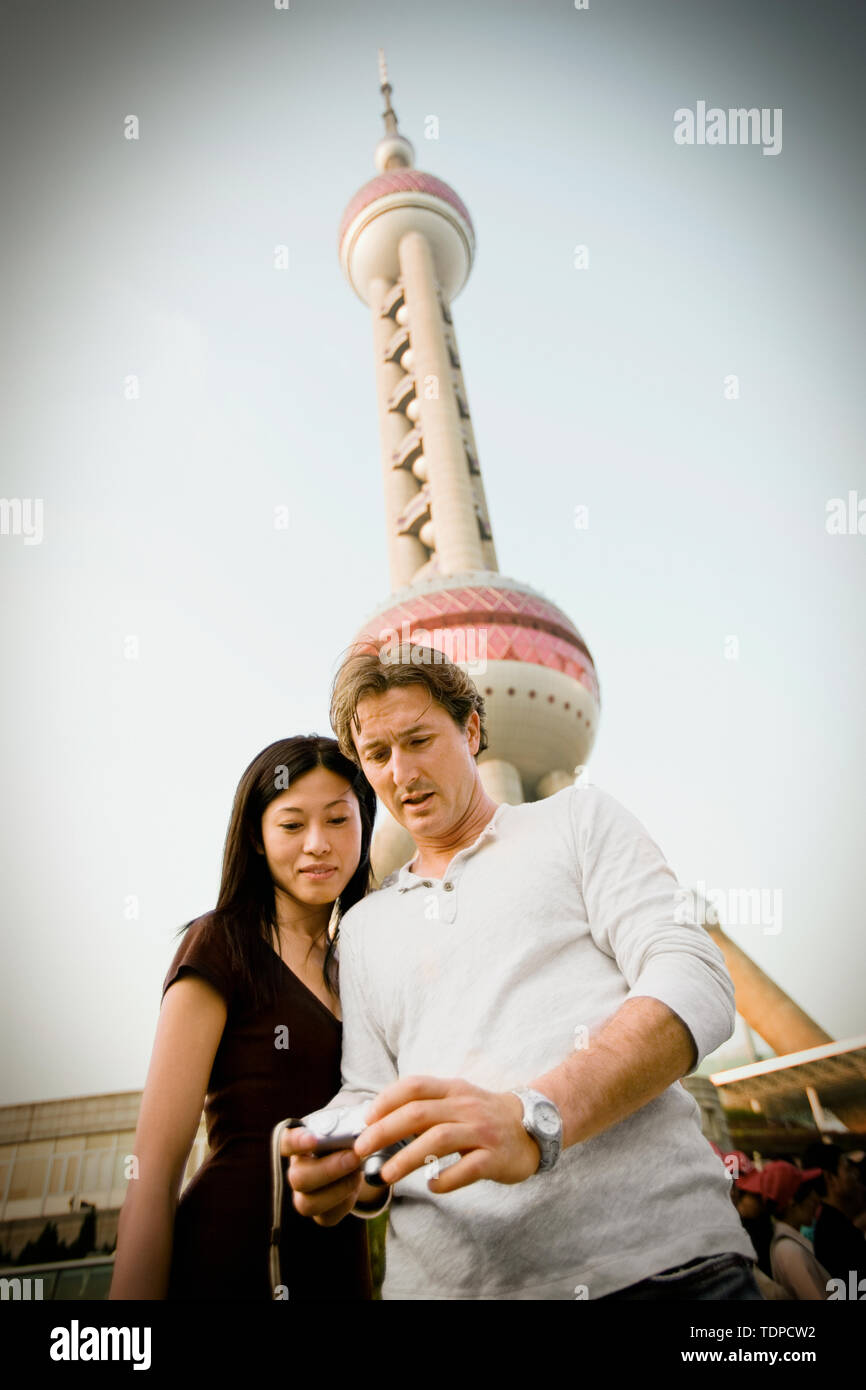 Mid-adult couple looking at the viewfinder of a digital camera while standing in front of a large tower in the city. Stock Photo