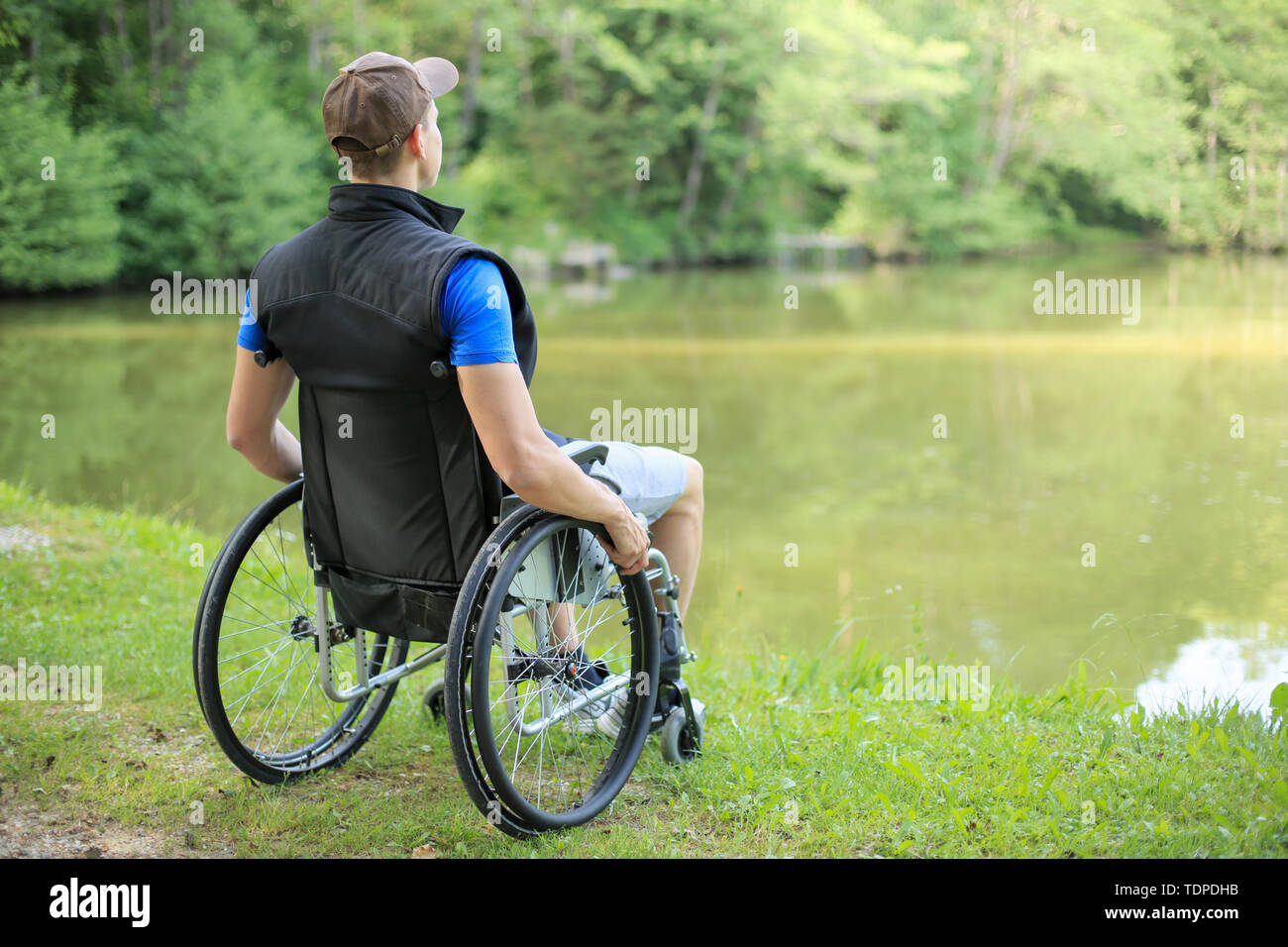 Happy and young or handicapped man sitting on a looking at beautiful lake in nature Stock - Alamy