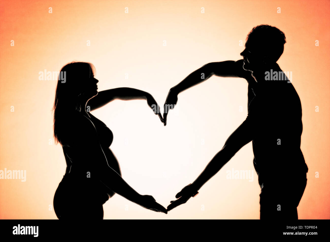 A silhouette in a studio of a couple who are having a baby and making a heart shape when the mother is well along in her pregnancy Stock Photo