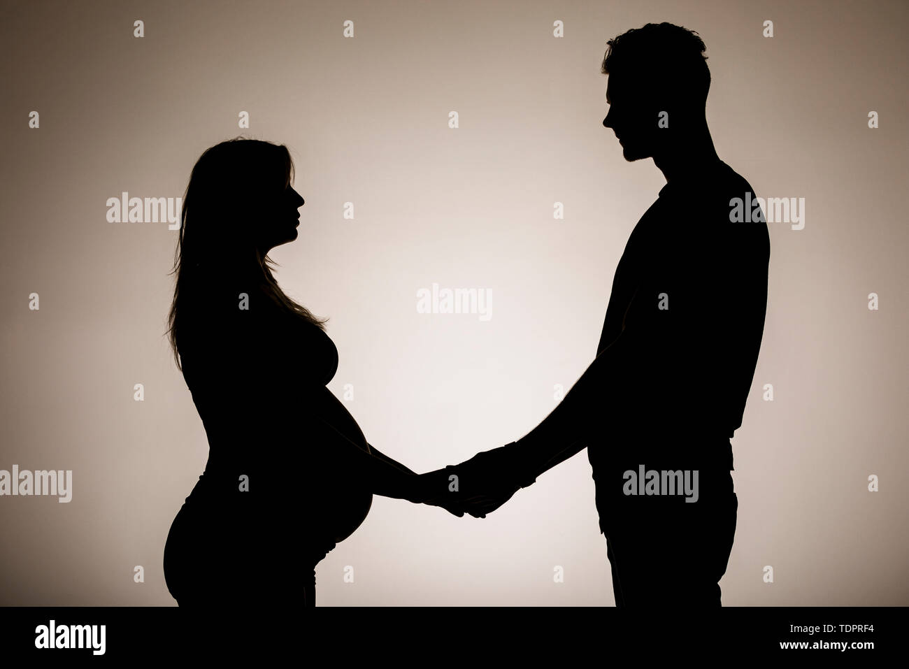 A silhouette in a studio of a couple who are having a baby and holding hands while the mother is well along in her pregnancy Stock Photo
