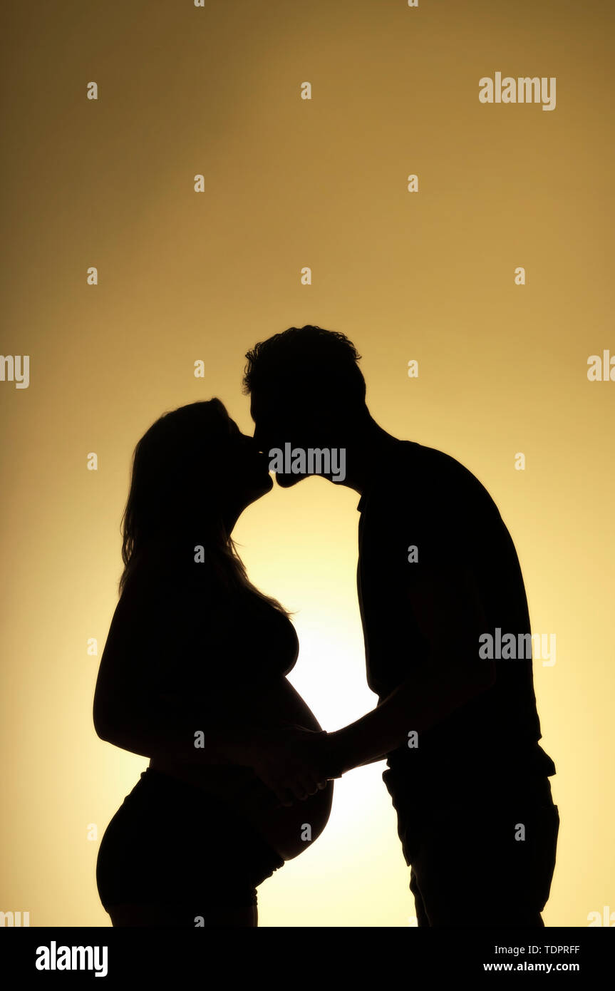 A silhouette in a studio of a couple  kissing who are having a baby and the mother is well along in her pregnancy; Edmonton, Alberta, Canada Stock Photo