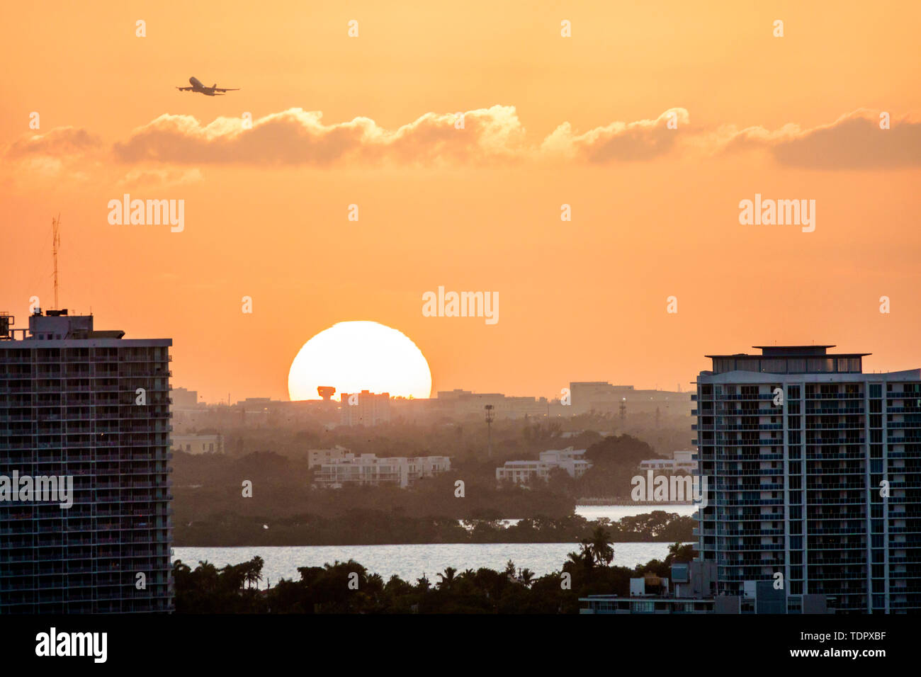 Miami Florida,Biscayne Bay water,North Bay water Village Island,sunset,city skyline cityscape,buildings,amber color sky,orb,jet aircraft commercial ai Stock Photo
