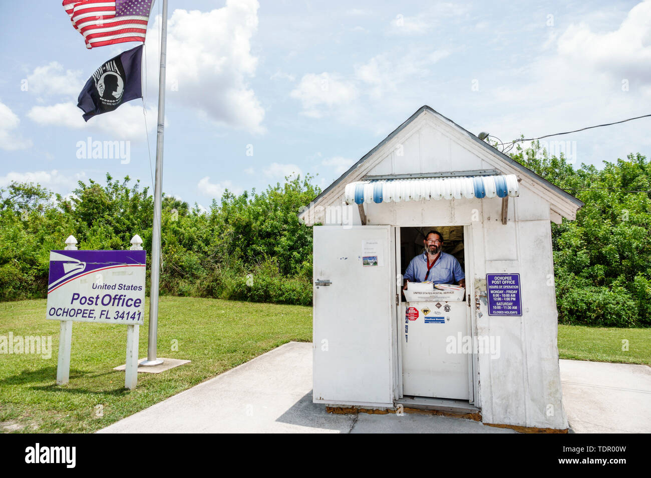 Florida,Ochopee,Everglades,Tamiami Trail,smallest post office,wood frame shed,post clerk,worker,man men male,service window,flag,FL190512074 Stock Photo
