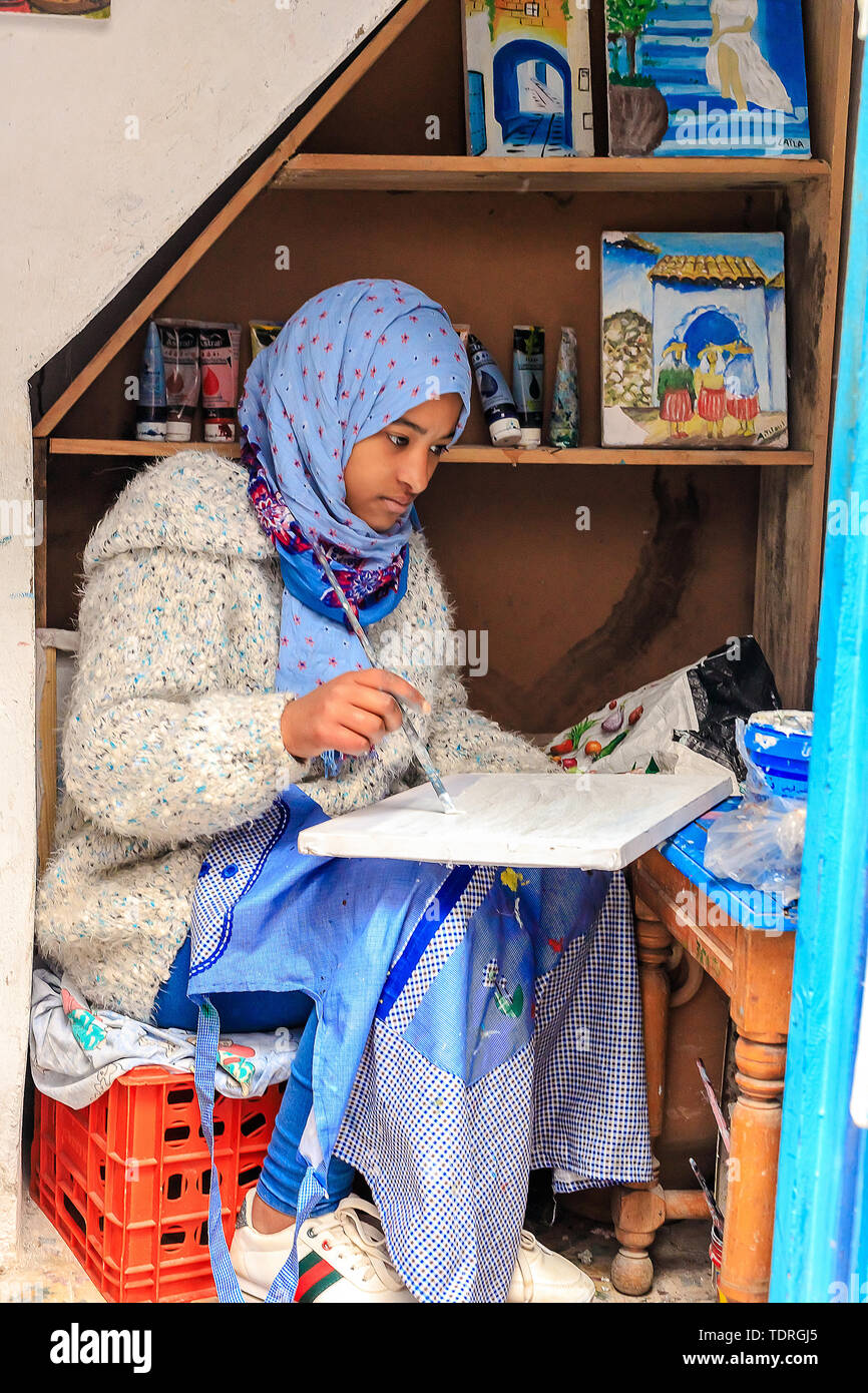 A beautiful Moroccan girl, a Muslim, street artist paints a picture with a brush in a small workshop. Chefchaouen, Morocco, Africa Stock Photo