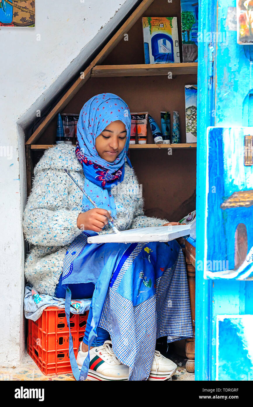 A beautiful Moroccan girl, a Muslim, street artist paints a picture with a brush in a small workshop. Chefchaouen, Morocco, Africa Stock Photo