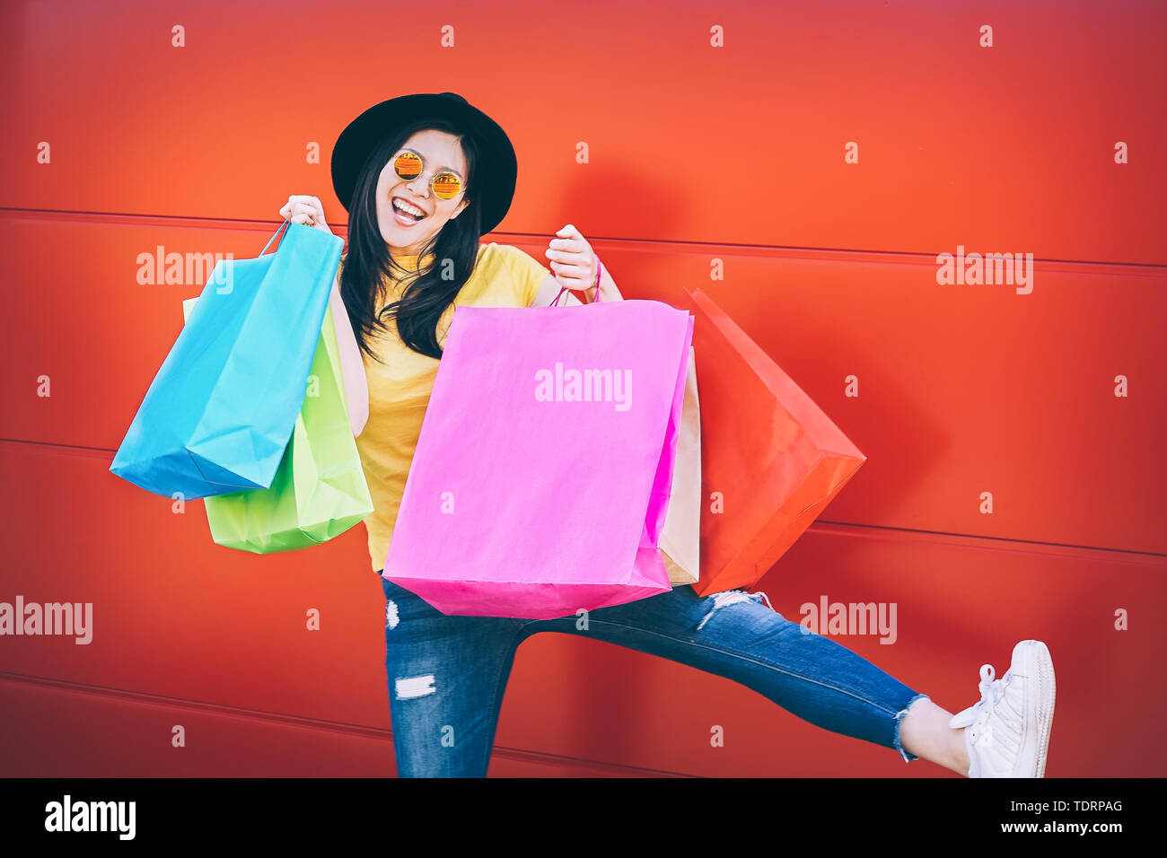 Happy fashion Asian woman doing shopping in mall center - Young Chinese girl having fun buying new clothes and celebrating against a red background Stock Photo