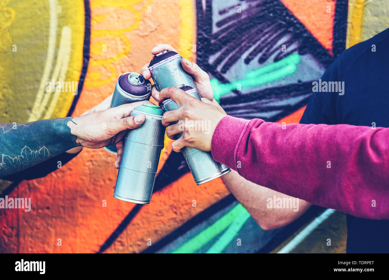 Group of graffiti artists stacking hands while holding spray color cans against mural background - Young painter at work Stock Photo