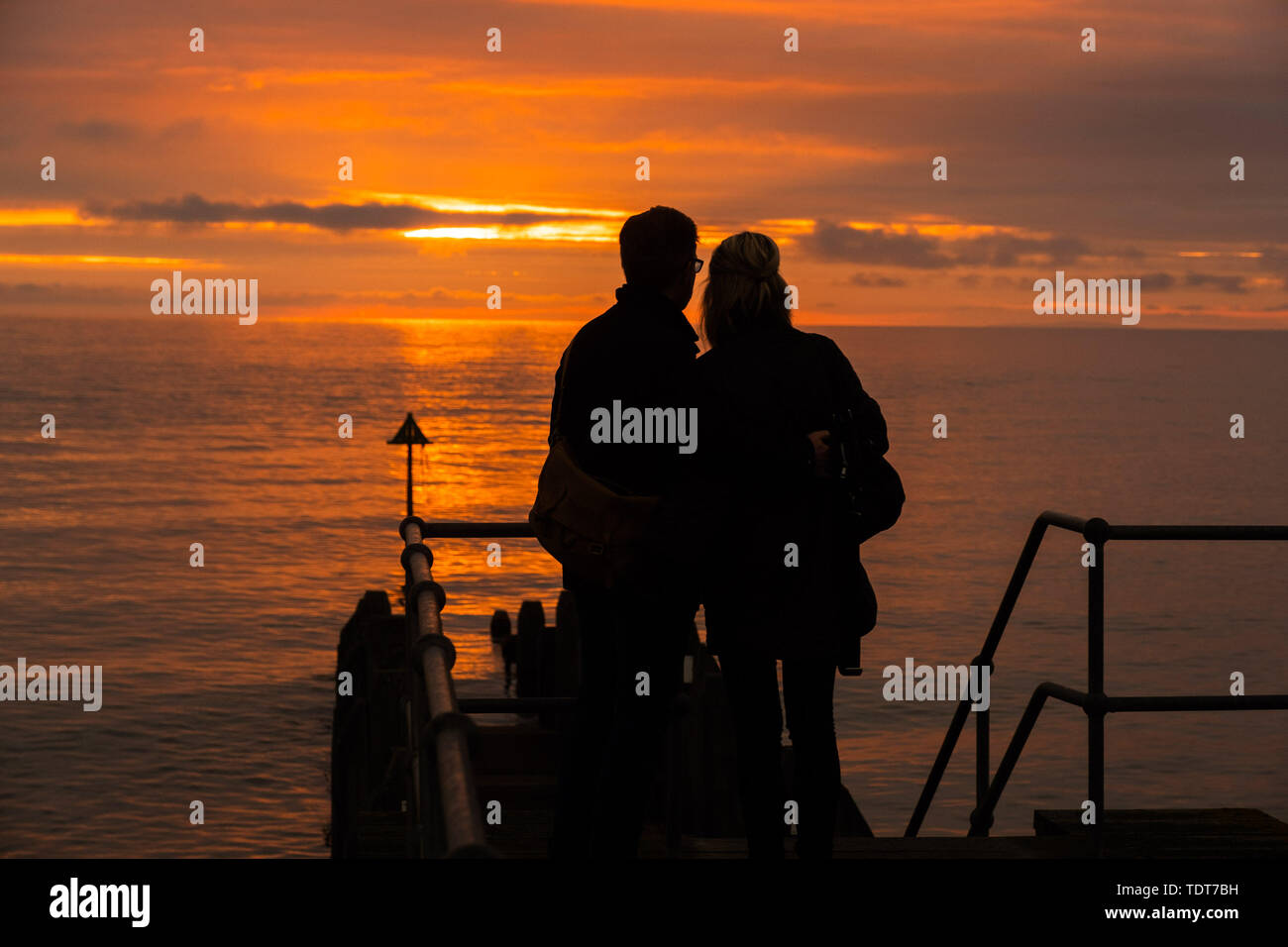 Aberystwyth Wales UK, Monday 17 June 2019  UK Weather:After day of showery rain and grey overcast skies, a couple are silhouetted as they watch the fiery sunset filling the sky over Cardigan Bay at Aberystwyth on the west wales coast.  photo credit: Keith Morris//Alamy Live News Stock Photo