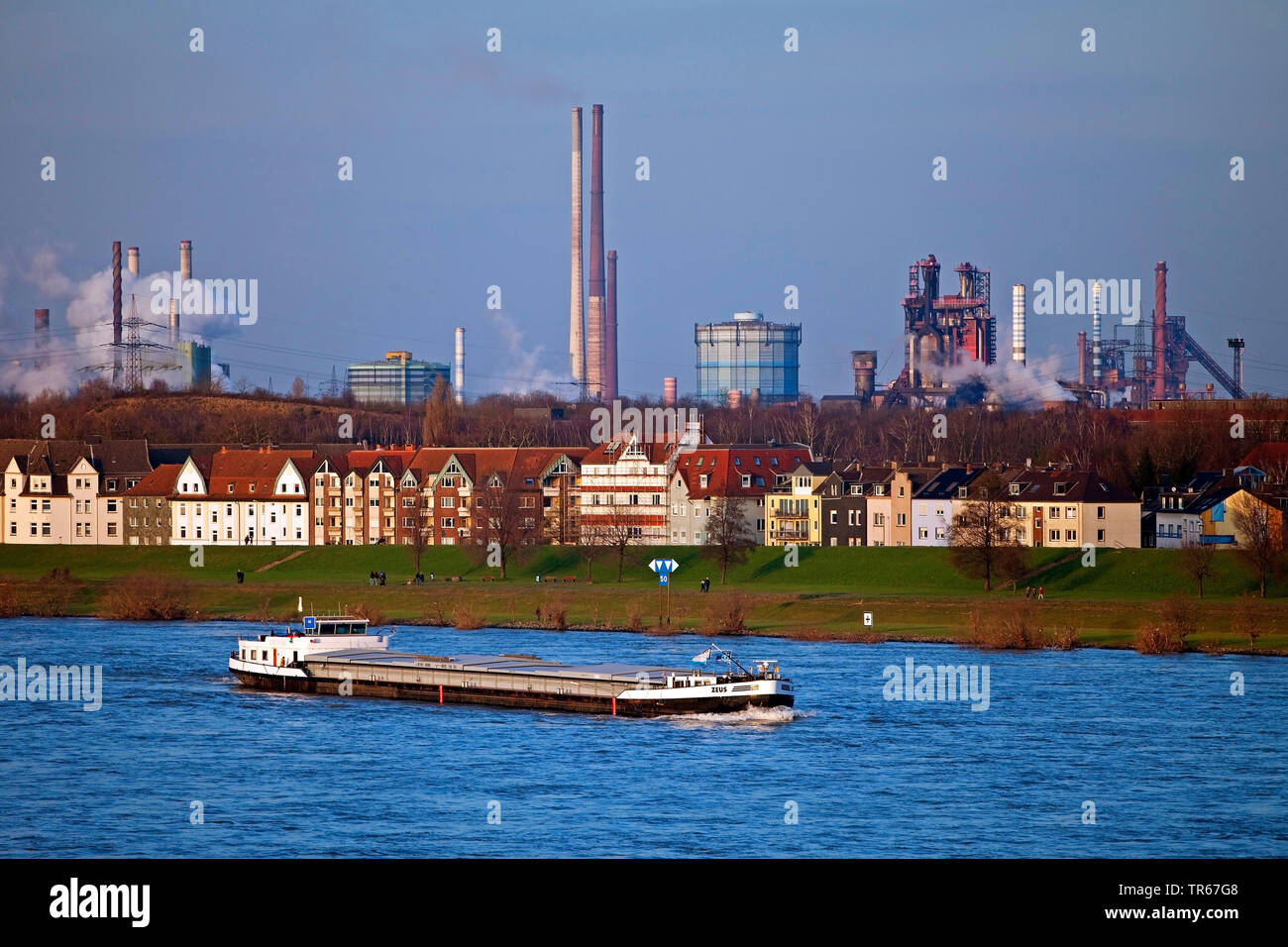 cargo ship on river Rhine, buildings and Thyssenkrupp industrial scenery in background, Germany, North Rhine-Westphalia, Ruhr Area, Duisburg Stock Photo