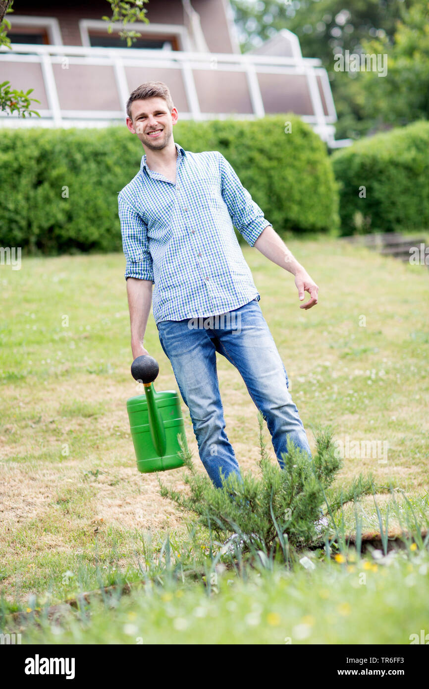 rosemary (Rosmarinus officinalis), young man watering rosemary in the garden, Germany Stock Photo
