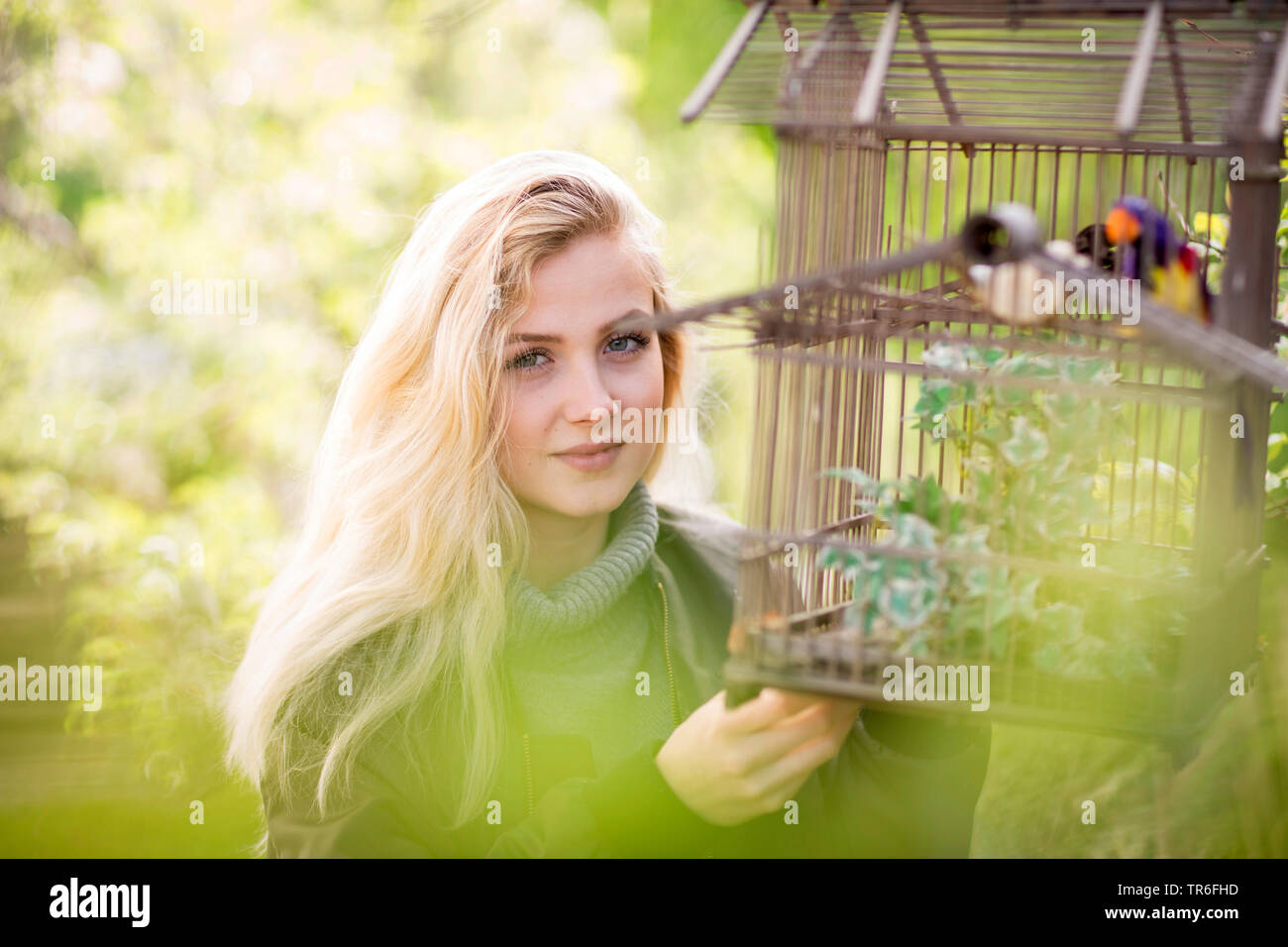 young blond woman with birdcage in a garden, Germany Stock Photo