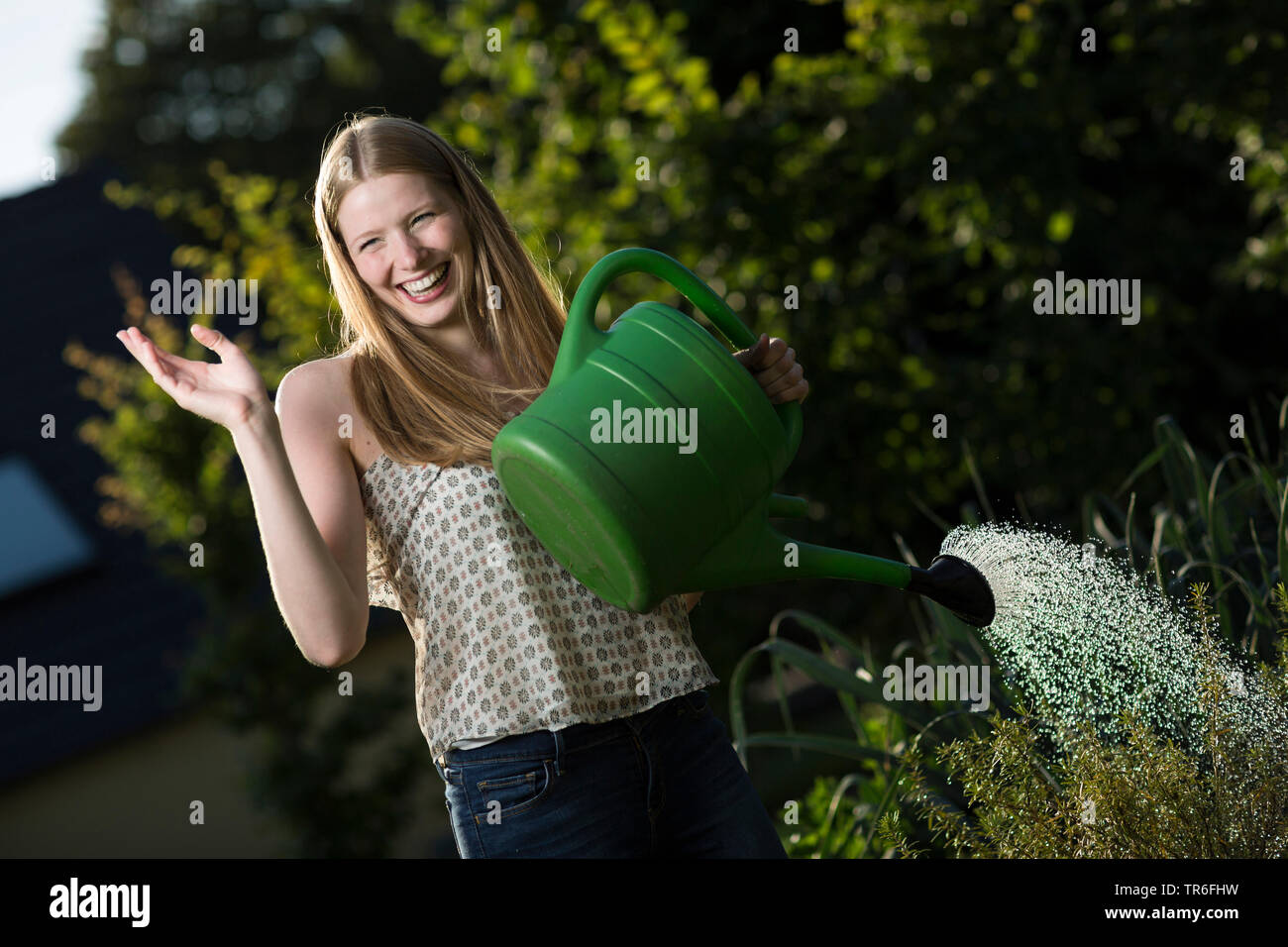 laughing young woman watering a vegetable patch with a watering can, Germany Stock Photo
