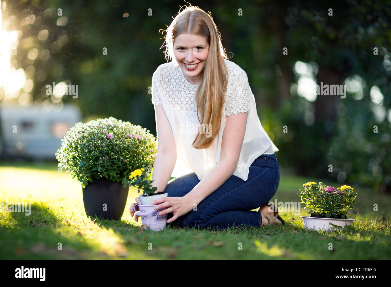 young blond woman sitting with asters on a lawn, Germany Stock Photo