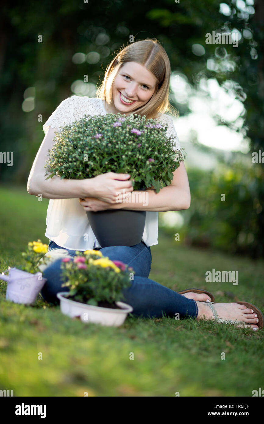 young blond woman sitting in a meadow with an aster in the arm , Germany Stock Photo