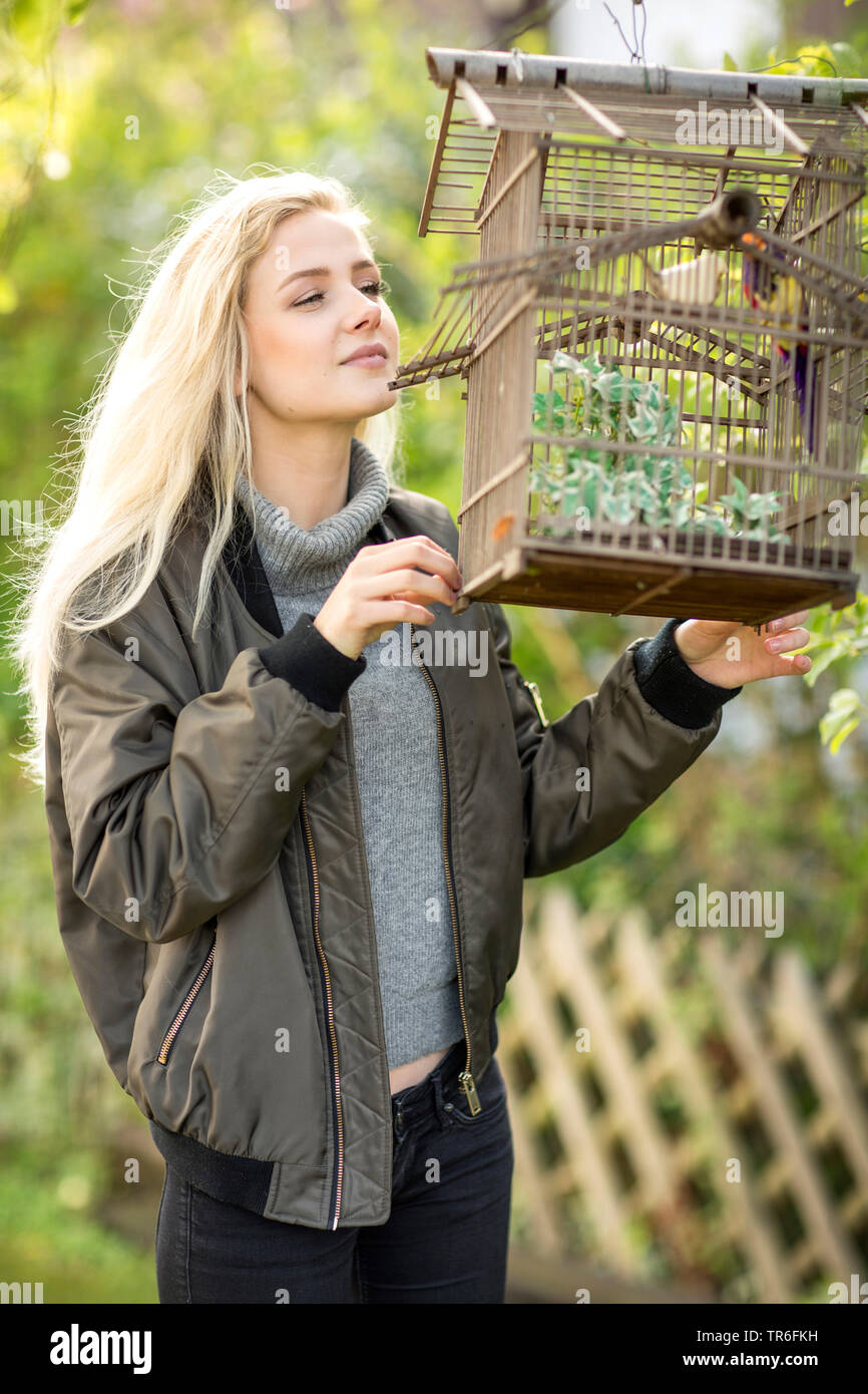 young blond woman looking outside a cagebird in a birdcage, Germany Stock Photo