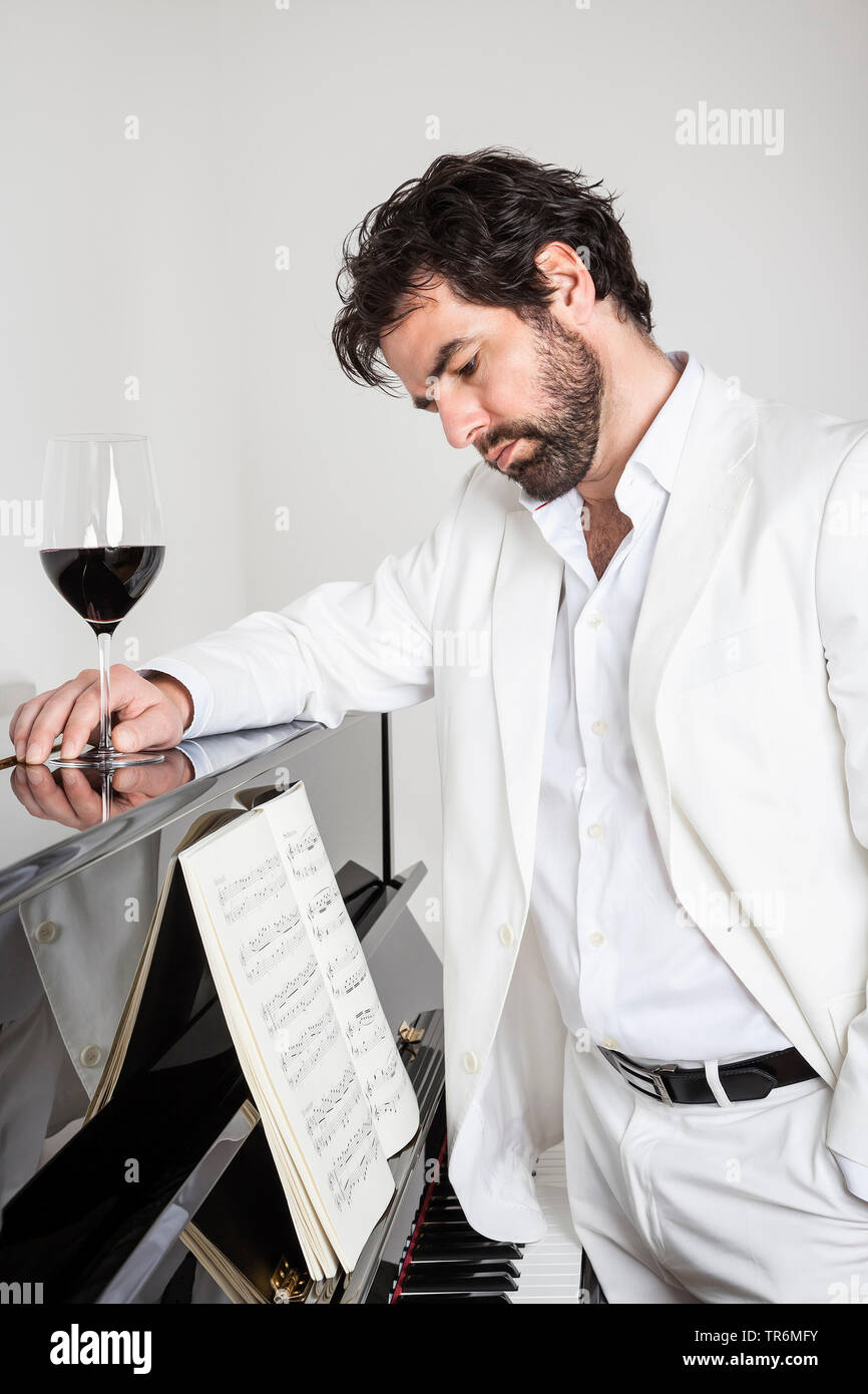 young man in white suit standing at a piano, Germany Stock Photo