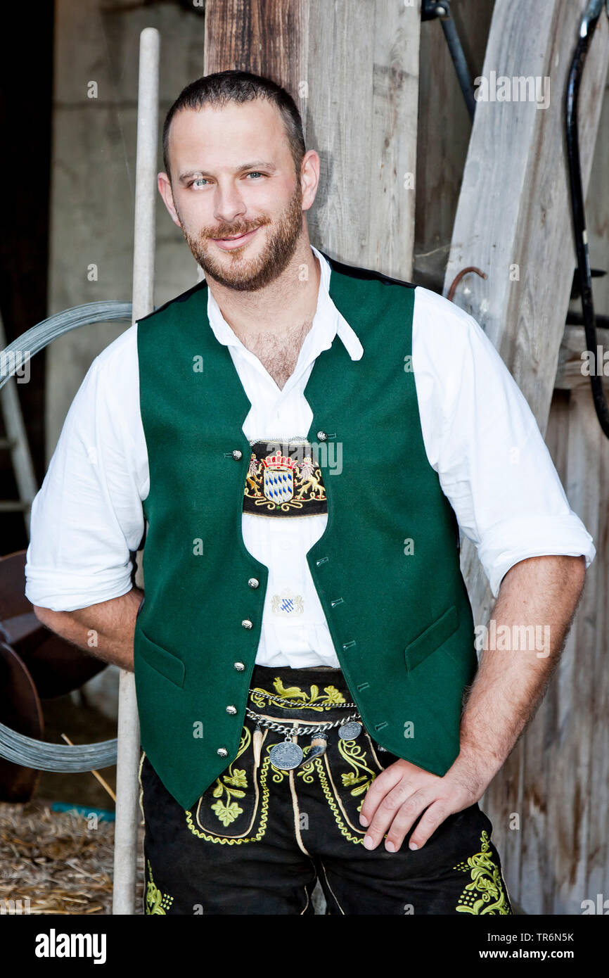 Stable Germany man in Bavarian traditional clothing standing leant at a wooden bar in ...