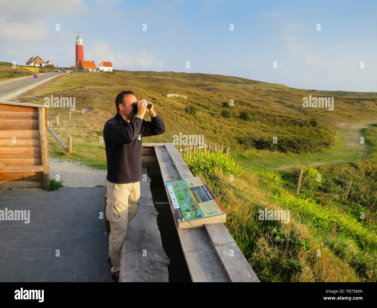 Man with binoculars at view point with lighthouse in background, Netherlands, Texel Stock Photo