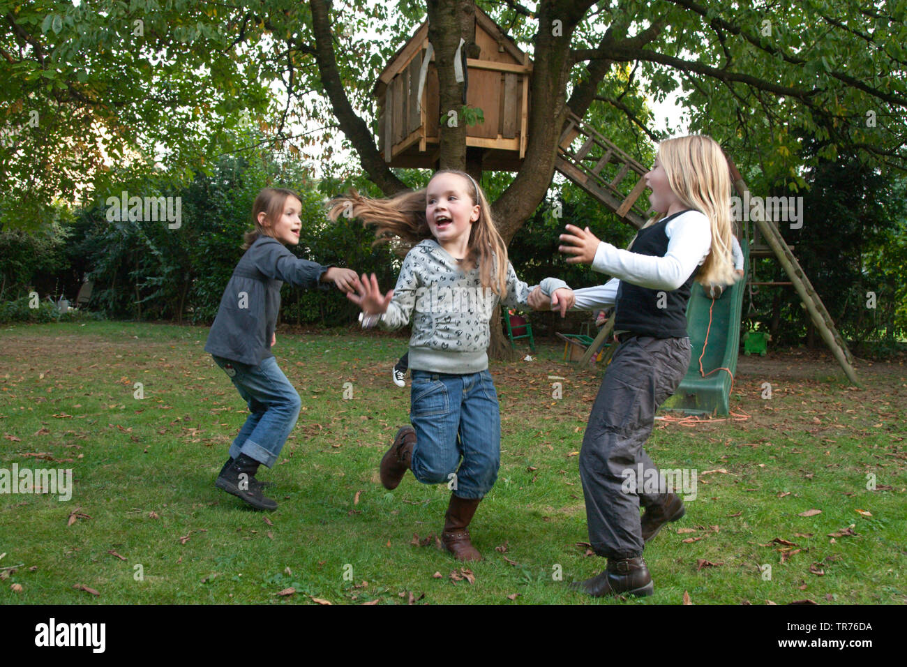 three children playing frolicsome near a tree house, Netherlands, Limburg Stock Photo