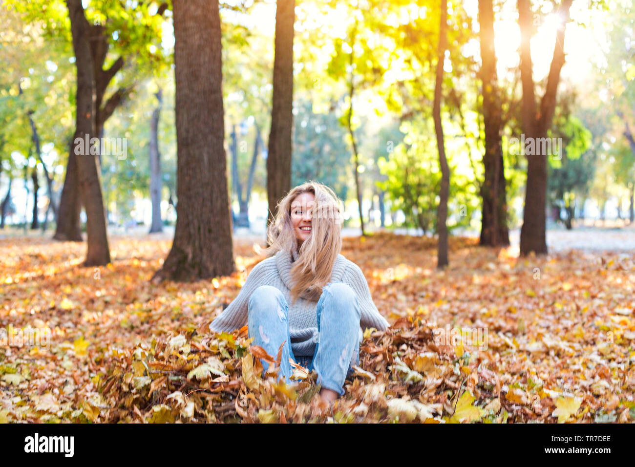 Happy blond girl posing in autumn park on yellow trees background. Have ...