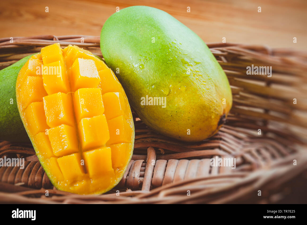 Close-up of fresh green Dashehari mangoes and its slice placed in wooden basket on wooden table. Stock Photo