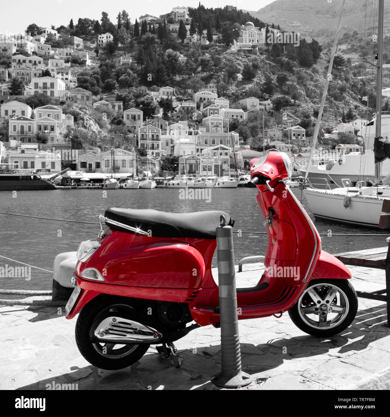 monochrome picture of the port of Symi in Greece with a red scooter in the foreground Stock Photo