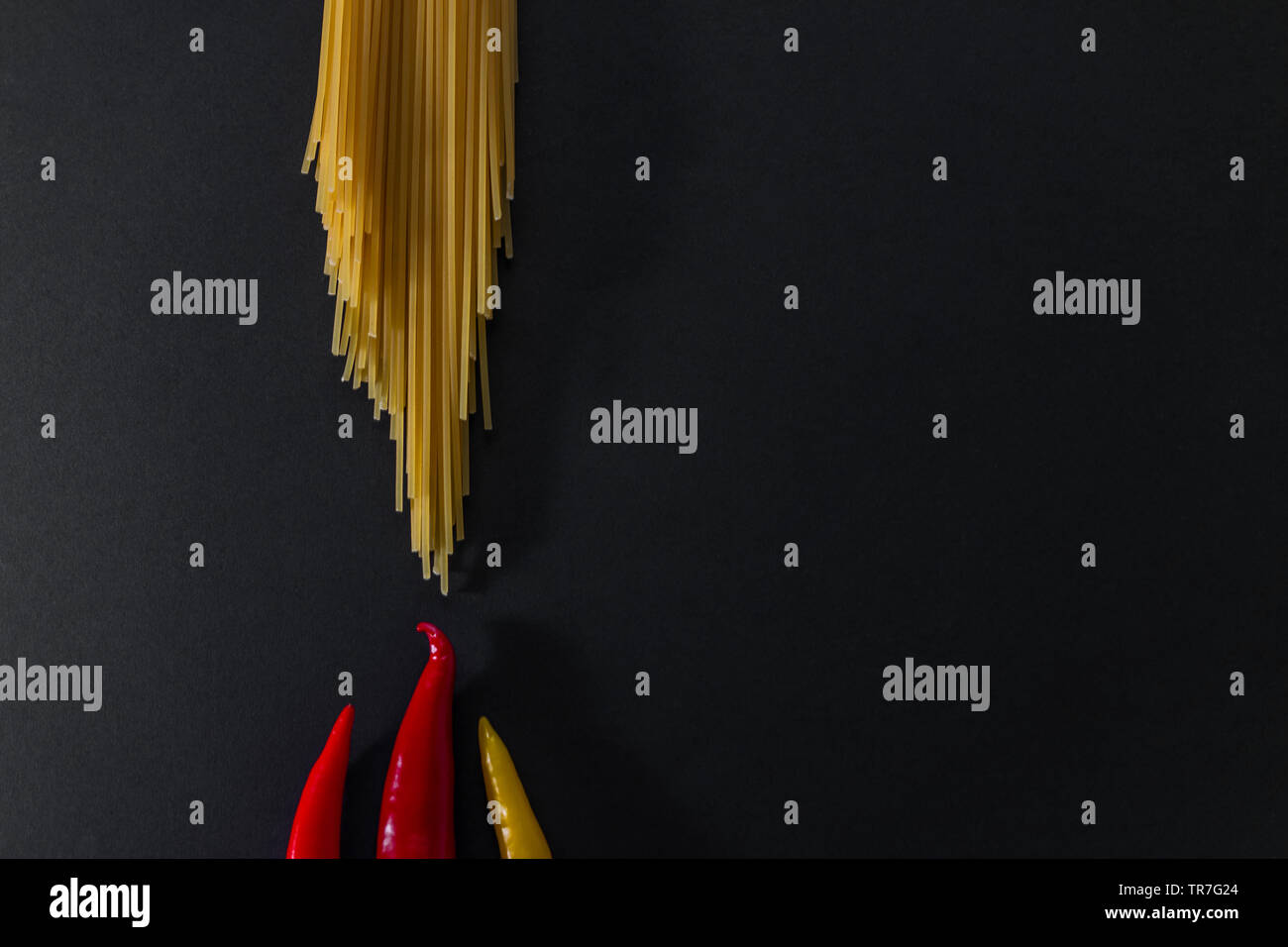 Raw spaghetti and fresh orange red yellow peppers on black surface. Flat lay view. Copy space. Cooking concept. Stock Photo
