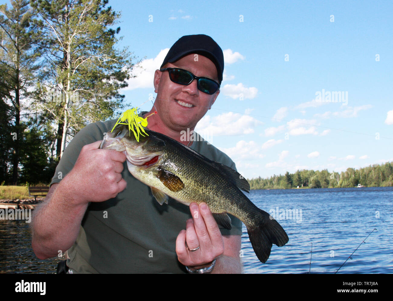 Proud fisherman in a boat with a Large Mouth Bass with a blue summer sky in the background Stock Photo