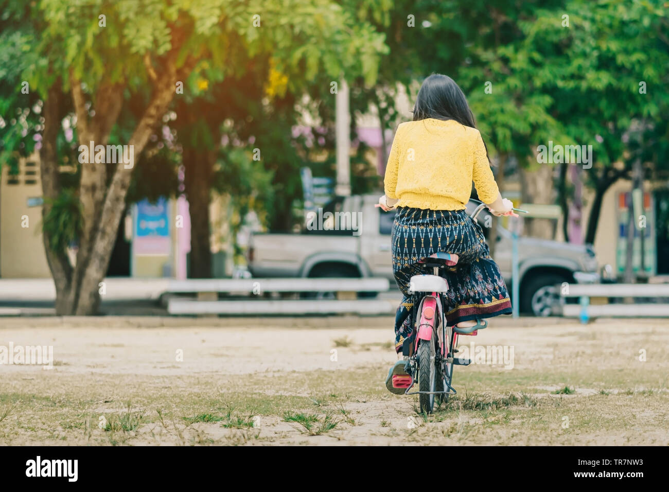 Back view of female teacher rides bicycle to teach students at ...
