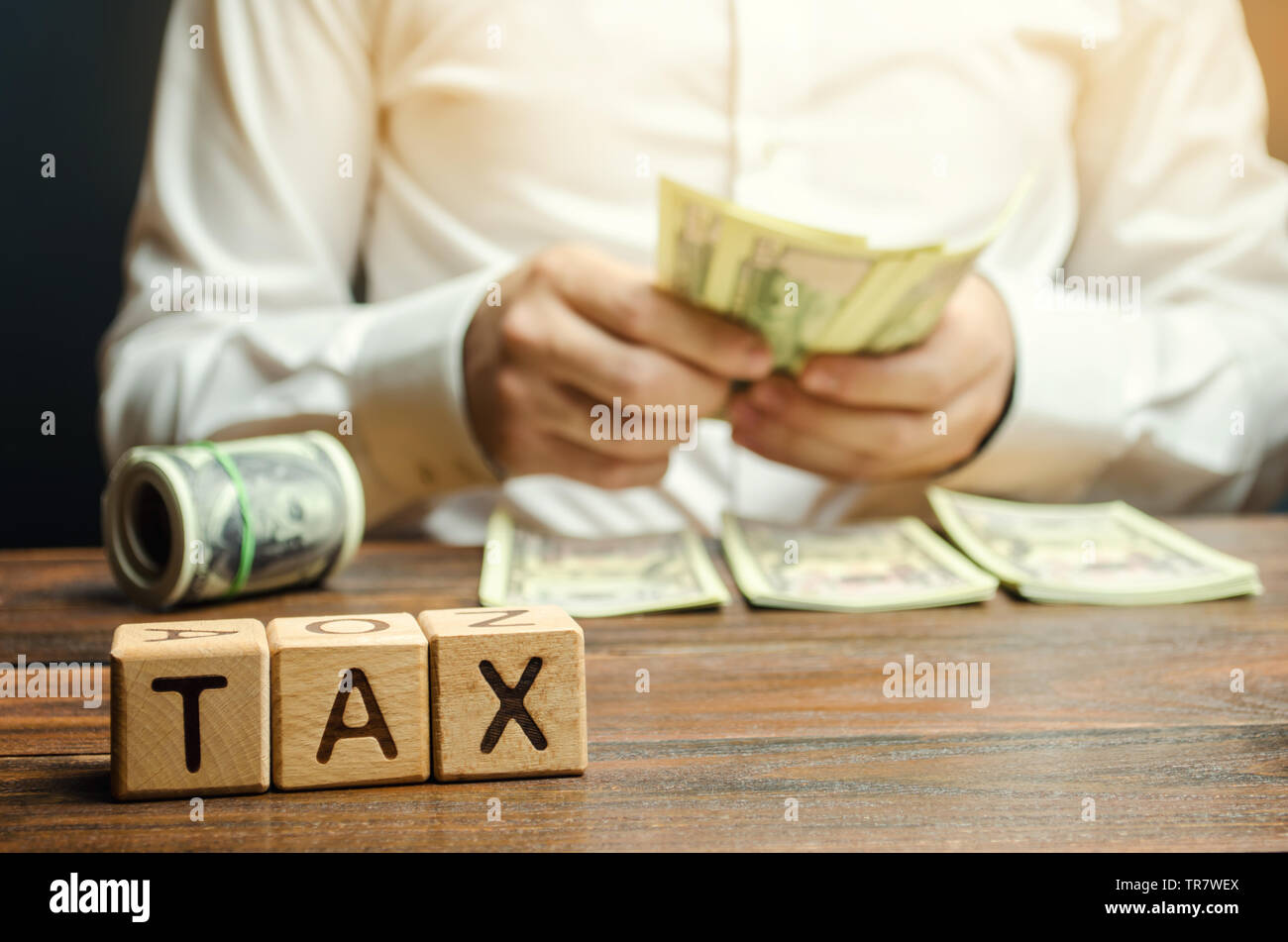 Wooden blocks with the word Tax and a businessman who counts money. The concept of time payment of taxes. Tax rates. Taxation / burden. Pay off debts. Stock Photo