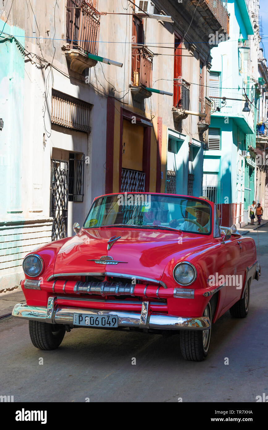 Classic American 1950's red car driving through a dilapidated street in the Old Town (Habana Vieja) of Havana, Cuba, Caribbean Stock Photo