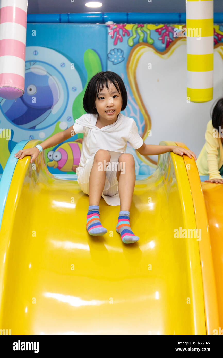 Asian Chinese little girl playing on the slide at indoor playground ...