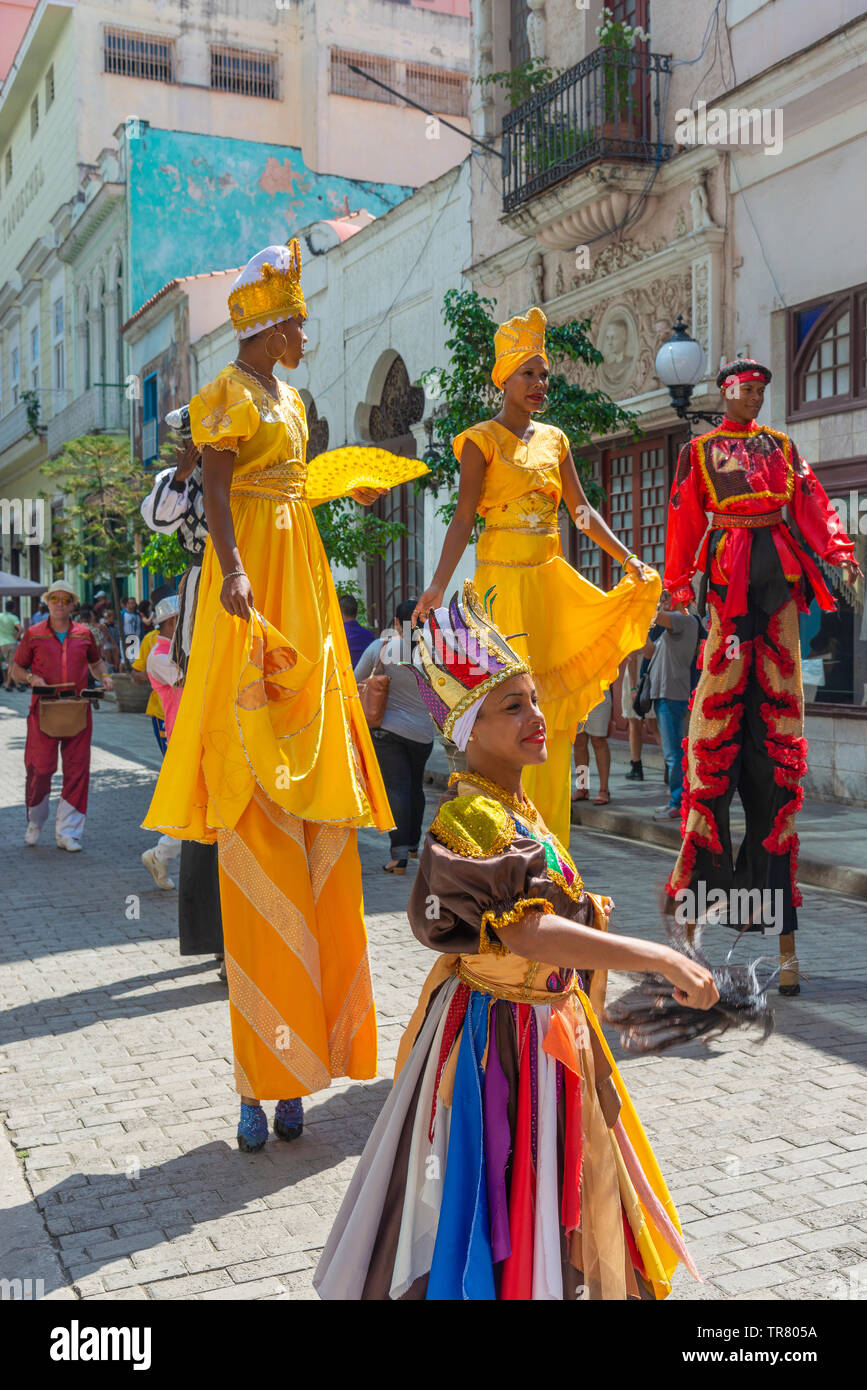 Colourfully dressed street performers in Old Havana, Cuba, some on stilts with a band playing following at the back. Stock Photo